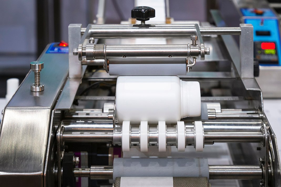 White plastic bottle on small tabletop bottle sticker labeling machine for medicine and pharmaceutical industry.