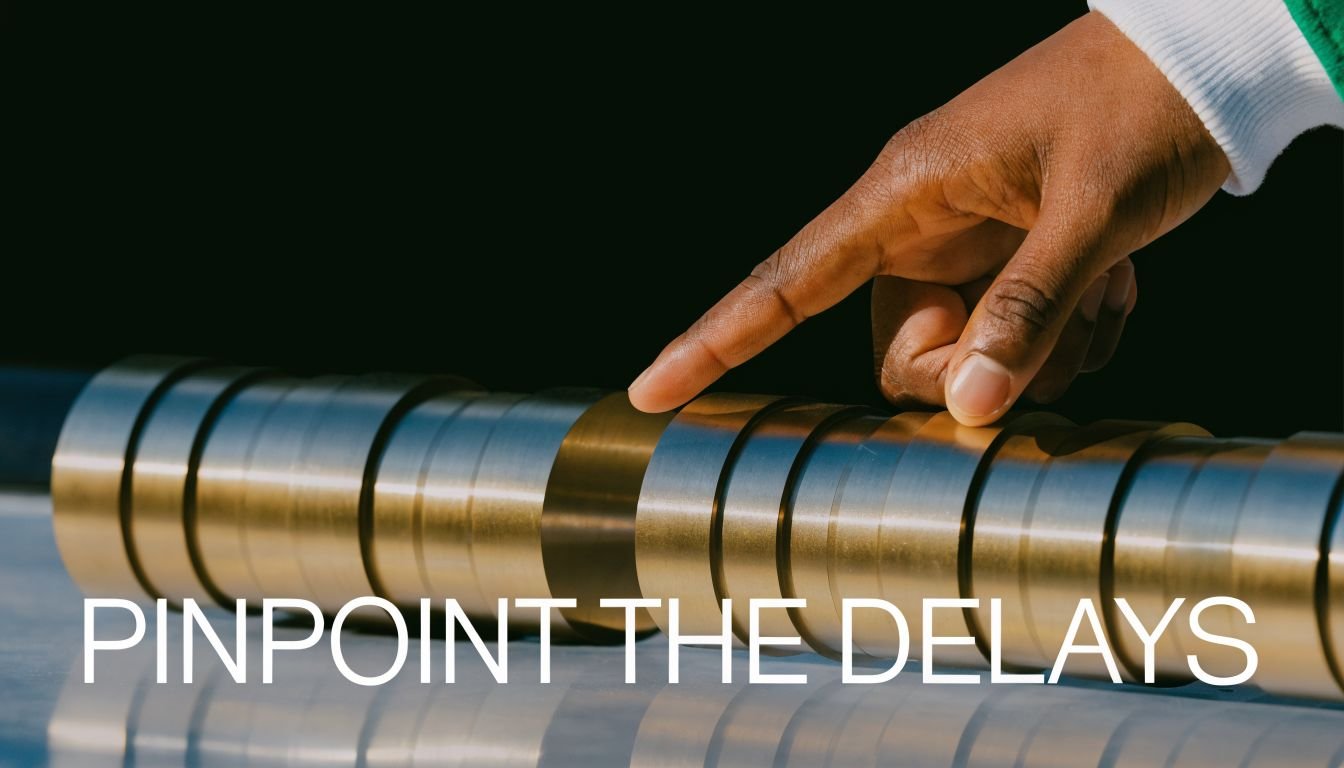 A hand pointing at a gap in a series of metallic cylindrical spacers to illustrate manufacturing delays.
