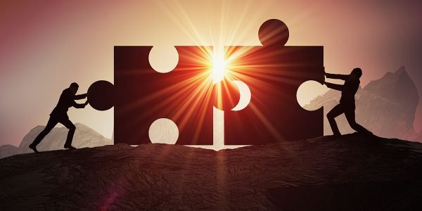 Teamwork, partnership and cooperation concept. Silhouettes of two businessman joining two pieces of puzzle together.