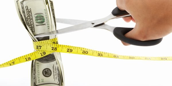 hand holding scissors to cut twined  US$100 bills with measuring tape over white background