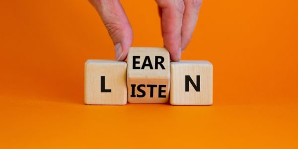Listen and learn symbol. Businessman turns a wooden cube and changes the word 'listen' to 'learn'. Beautiful orange background, copy space. Business, education and listen and learn concept.